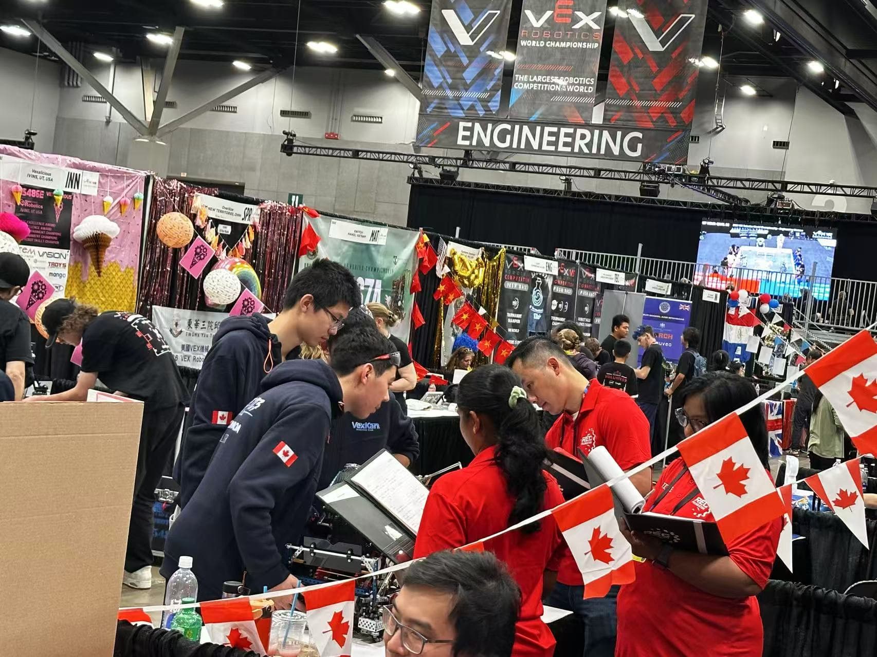 The pit hall at the World Championship, a clubber working at the team's booth under the Engineering sign with team banners down the row.