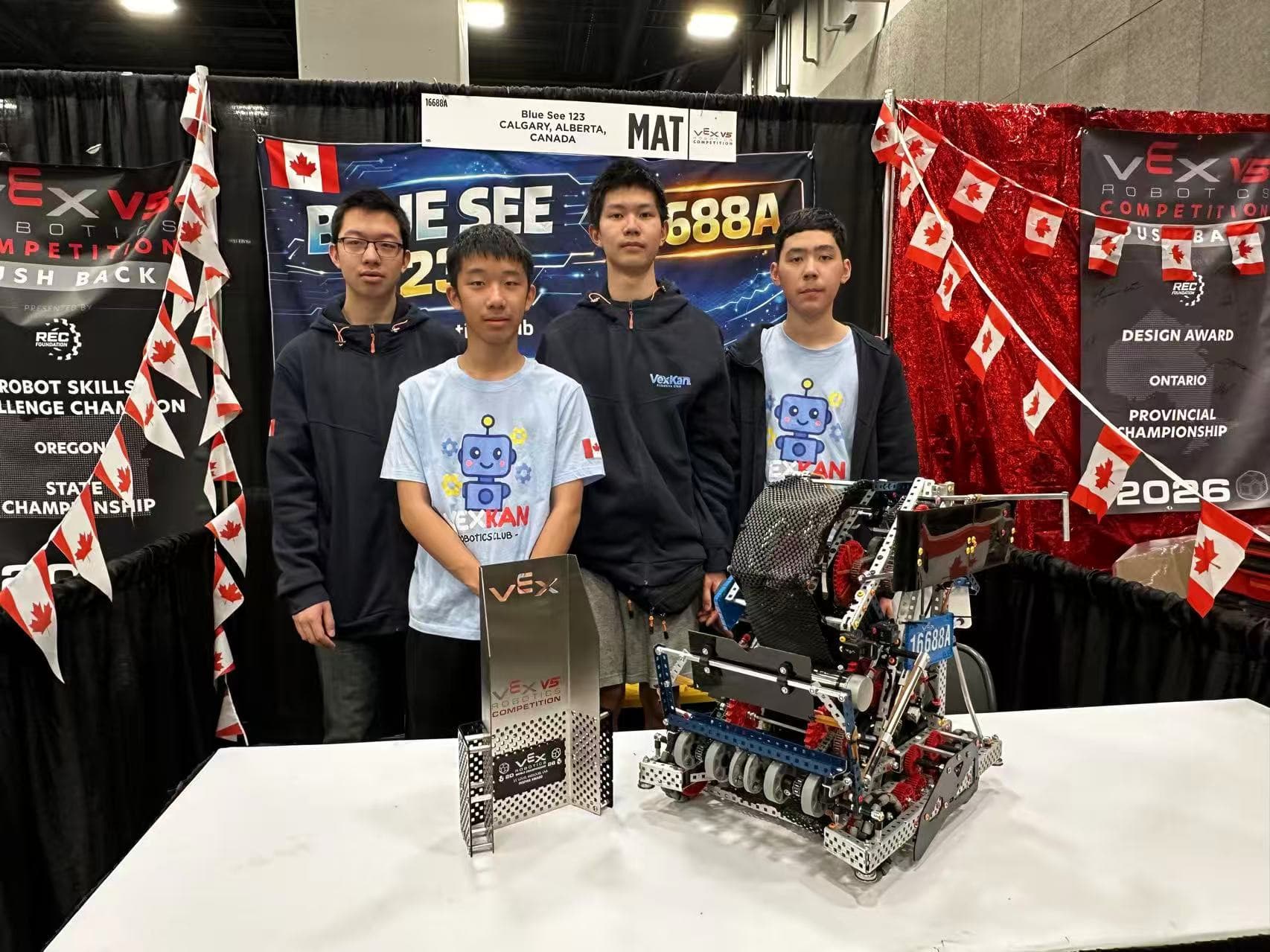 Four clubbers standing behind their V5 robot and its award at the team's pit, Canadian flags strung across the booth.