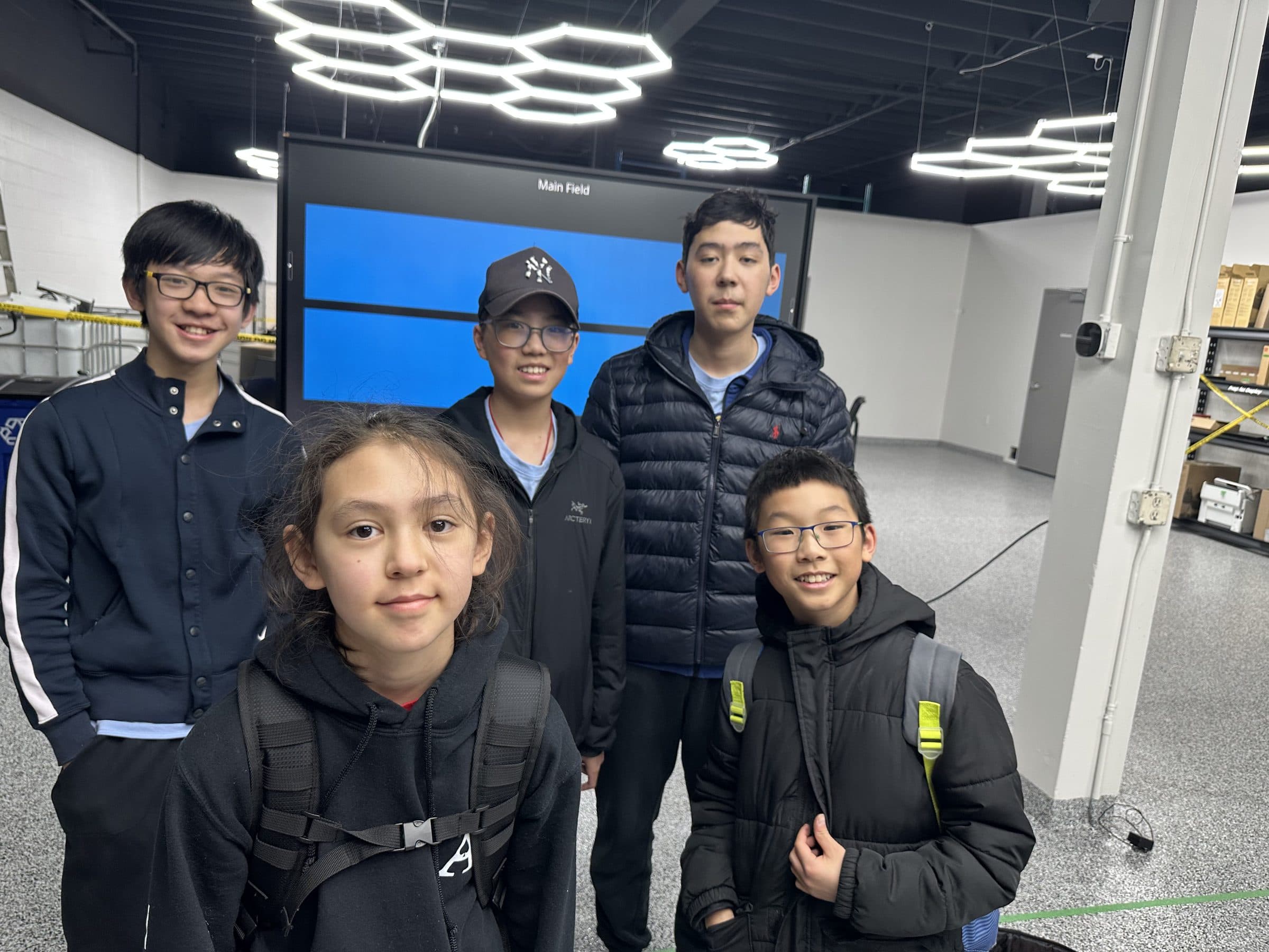 Five clubbers standing together in the club's practice space in front of the screen that shows the main field.
