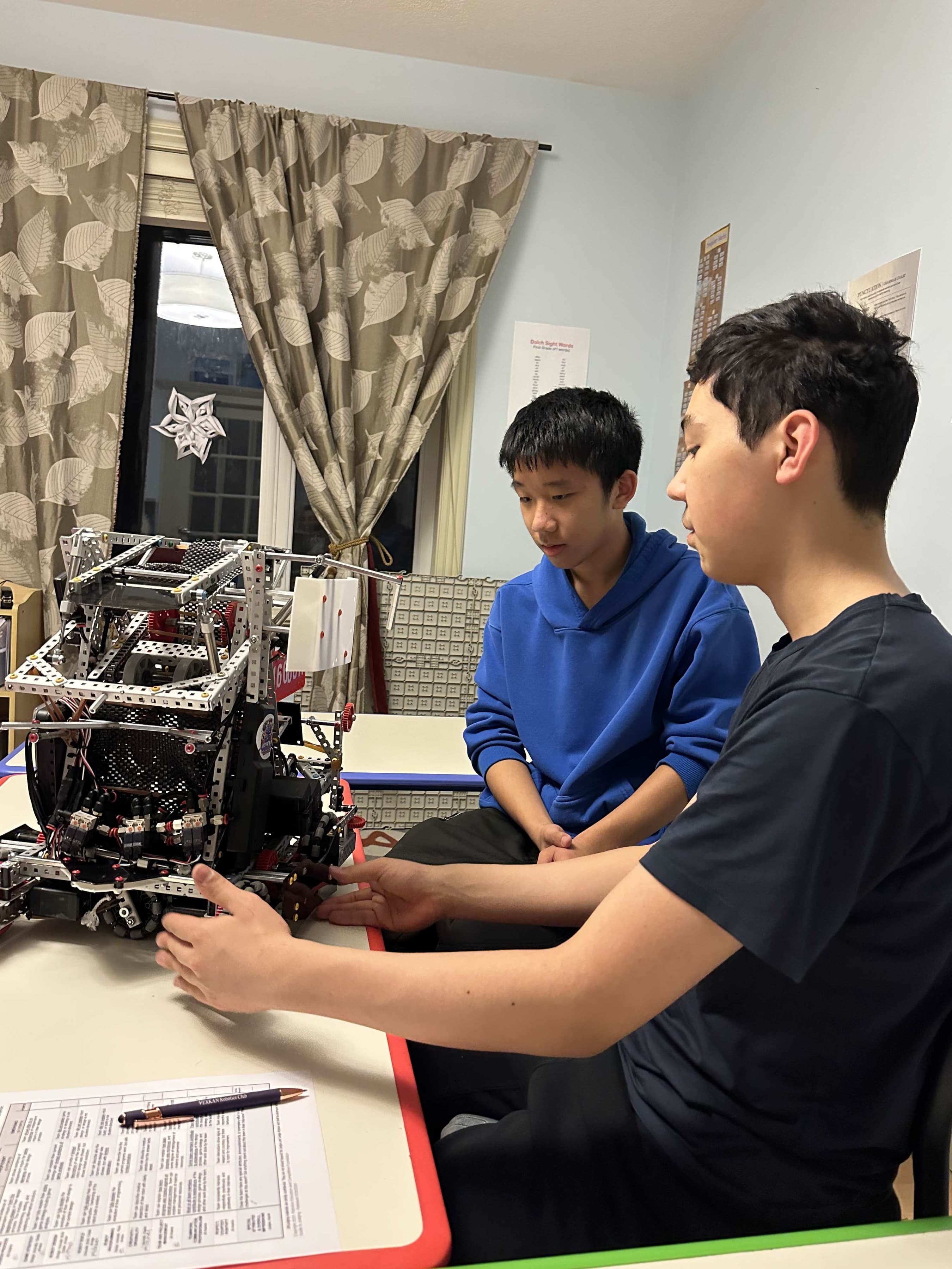 Two students at a table going over a V5 robot together, with a scoring sheet and a club pen in front of them.