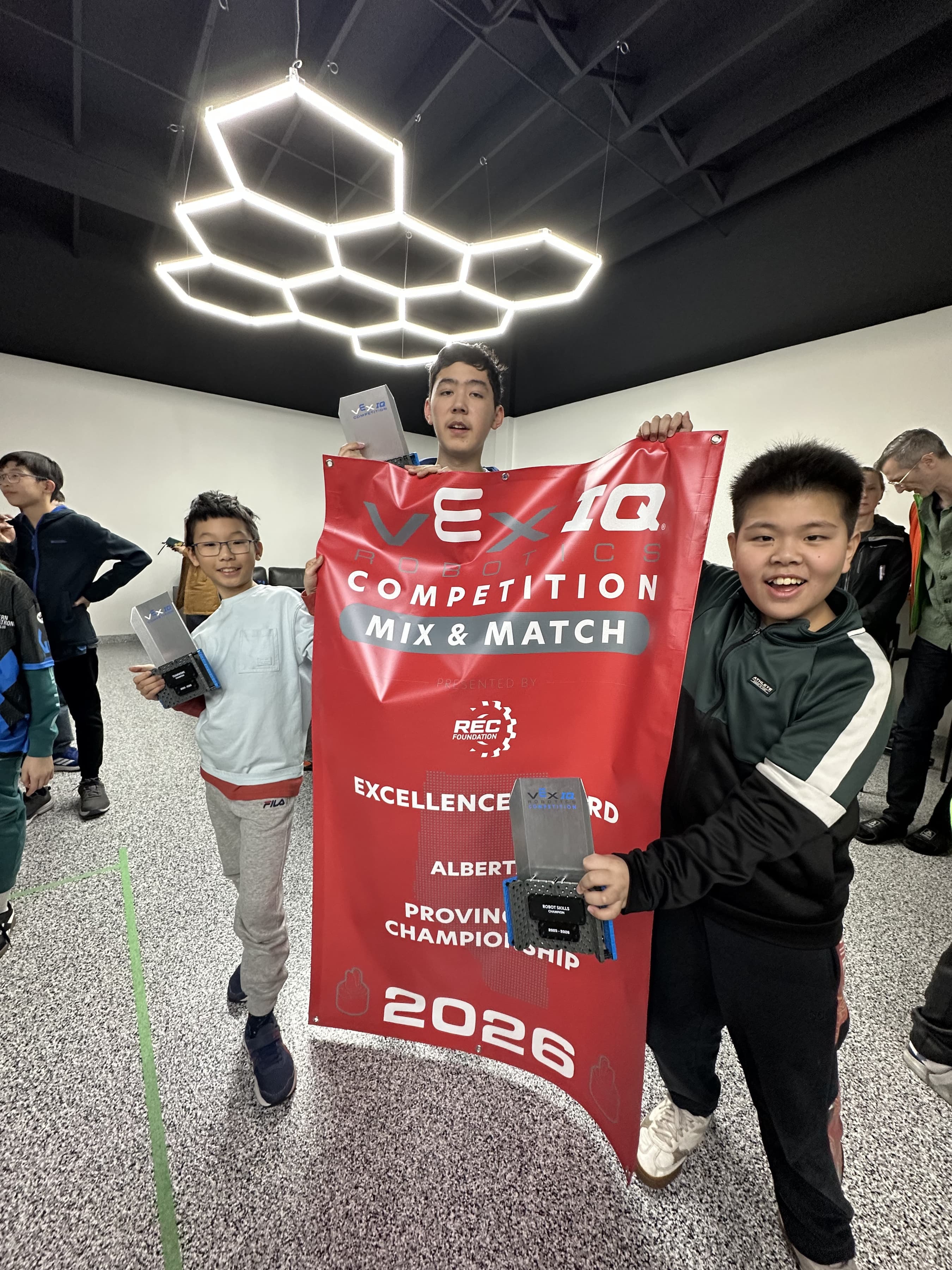 Members of 595Y holding up the Excellence Award banner from the Alberta provincial championship, with the Robot Skills Champion trophy.