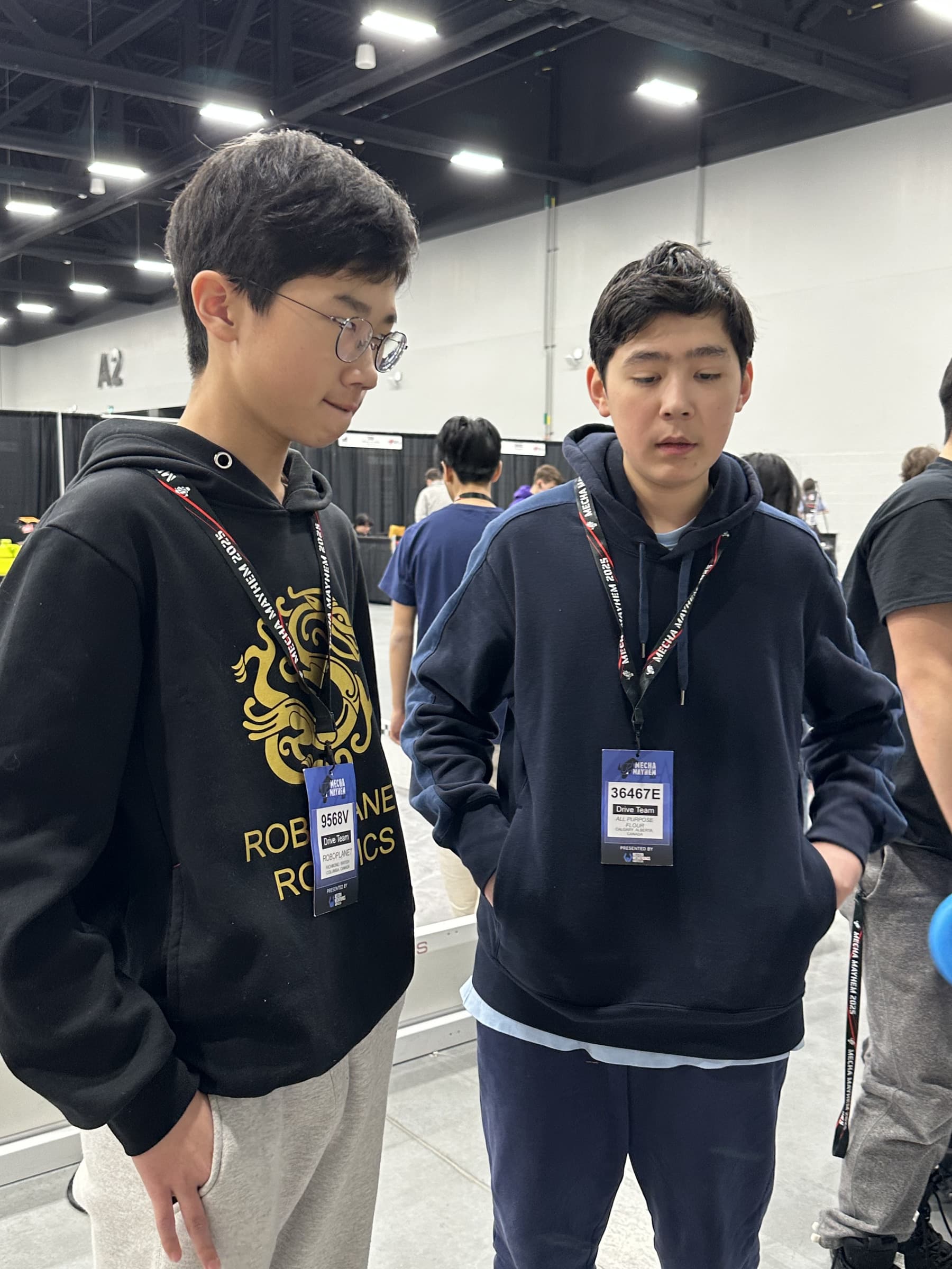 Two students from different clubs standing side by side in the hall, drive team badges hanging around their necks.