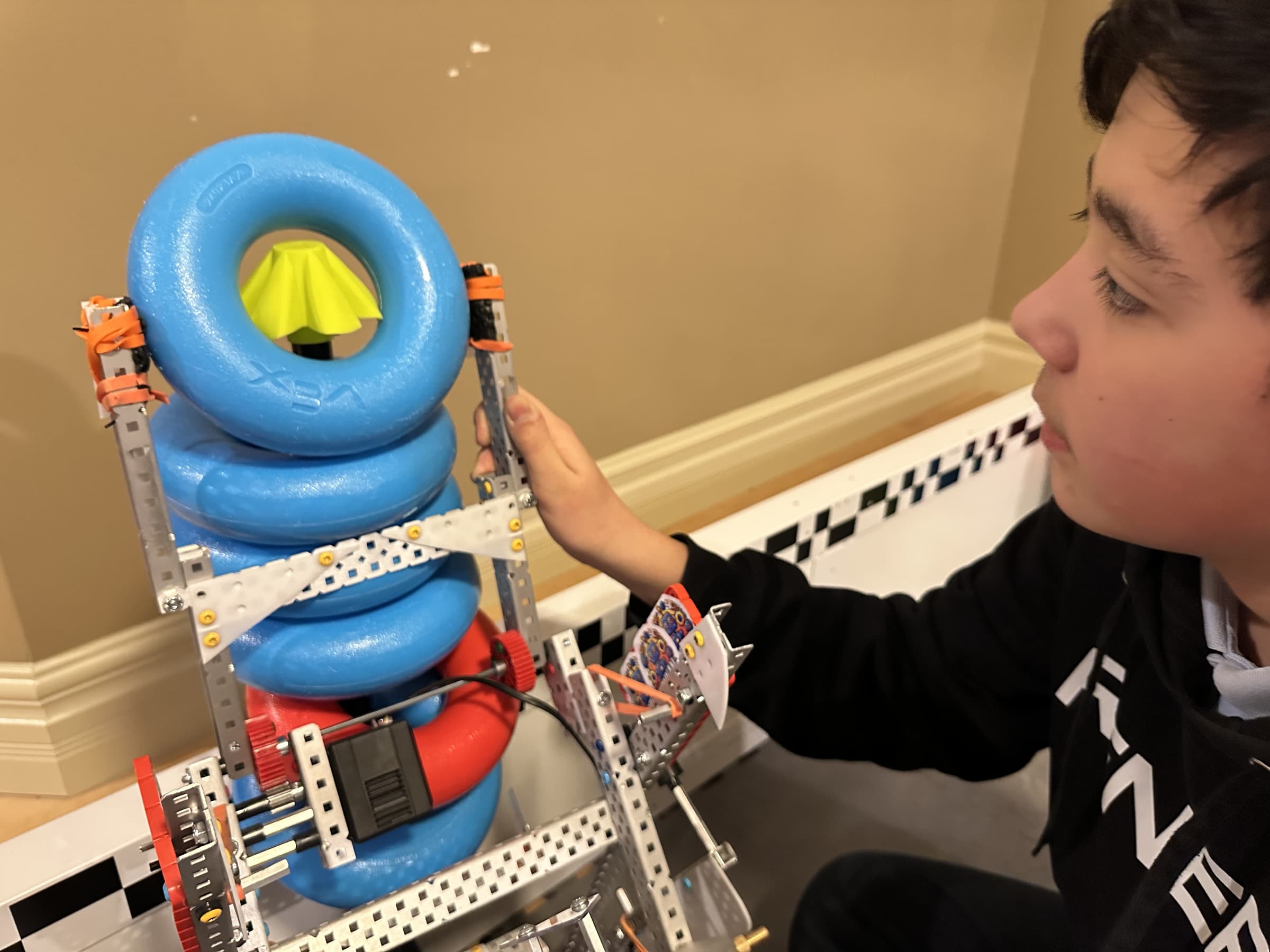 A clubber holding a stack of blue game rings on the robot's lift, checking how the mechanism holds them.