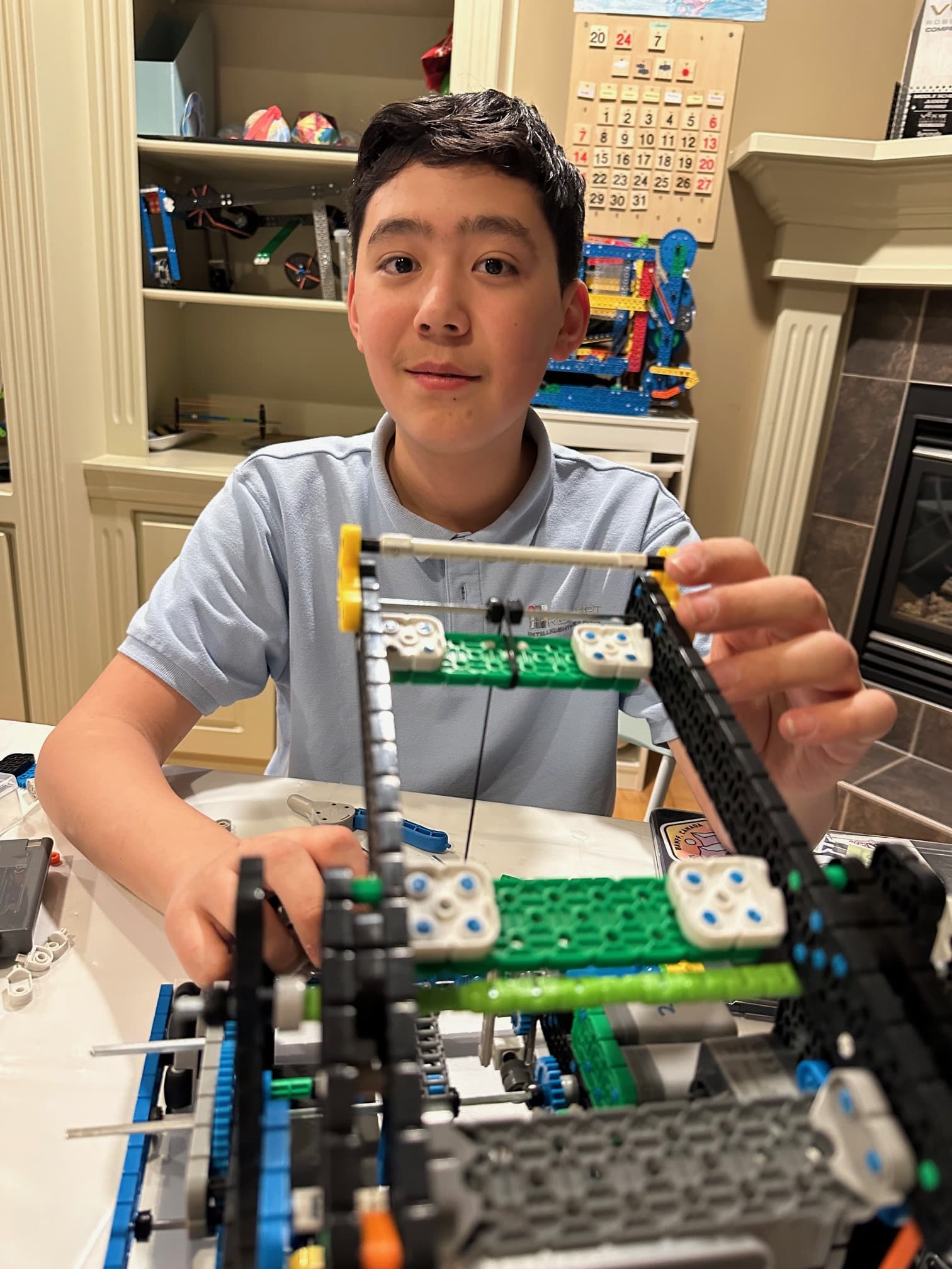 A clubber at the kitchen table building the lift on a V5 robot, an earlier robot on the shelf behind him.