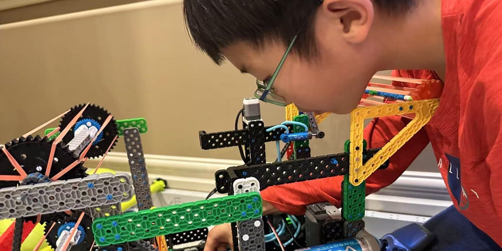 A clubber leaning in close to check a half-built VEX IQ robot on the table in front of him.