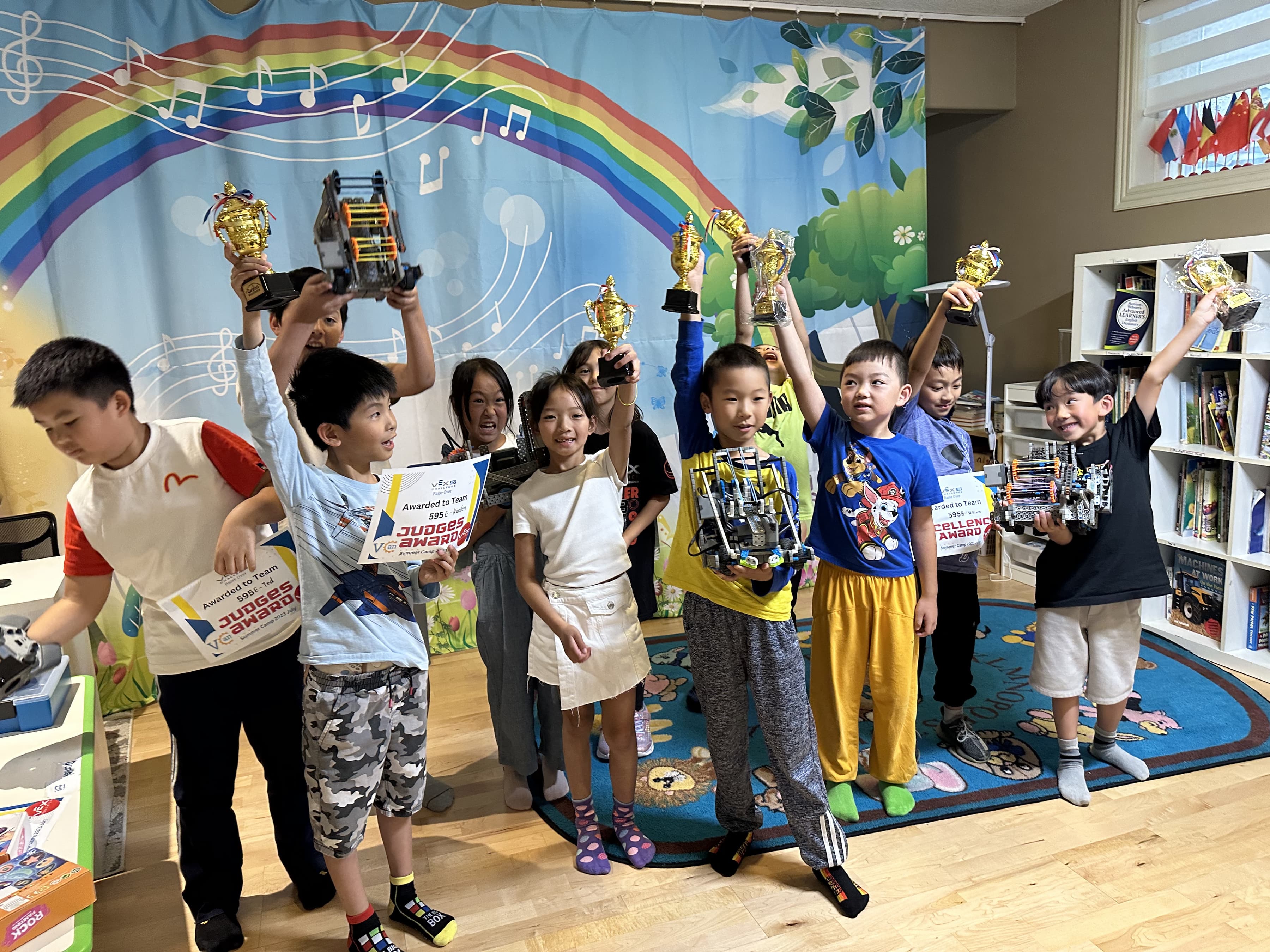Young clubbers holding gold trophies and certificates above their heads at the end of a summer camp.