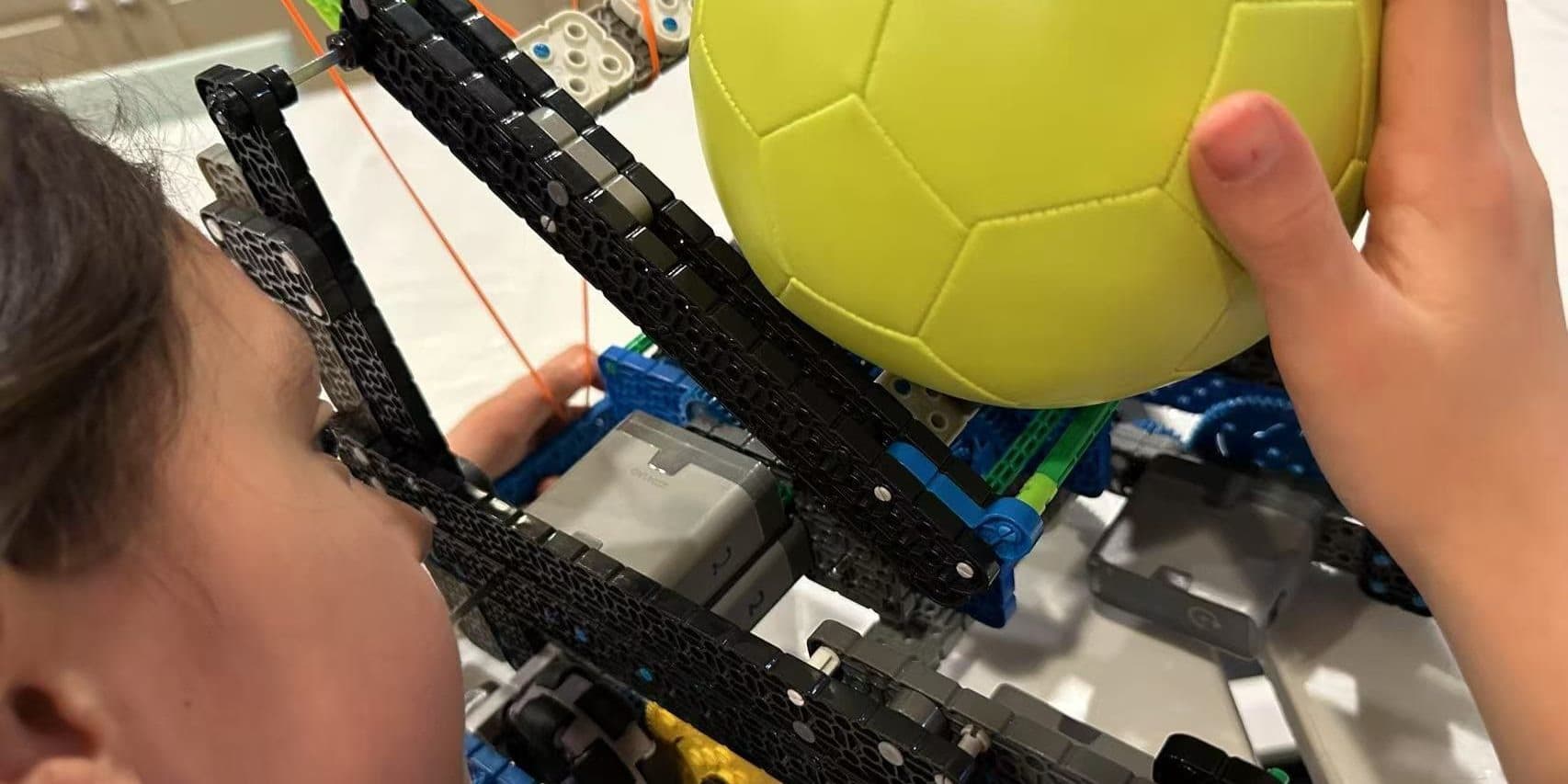 A close-up of a clubber's hand holding a game ball against the arm of a VEX IQ robot.