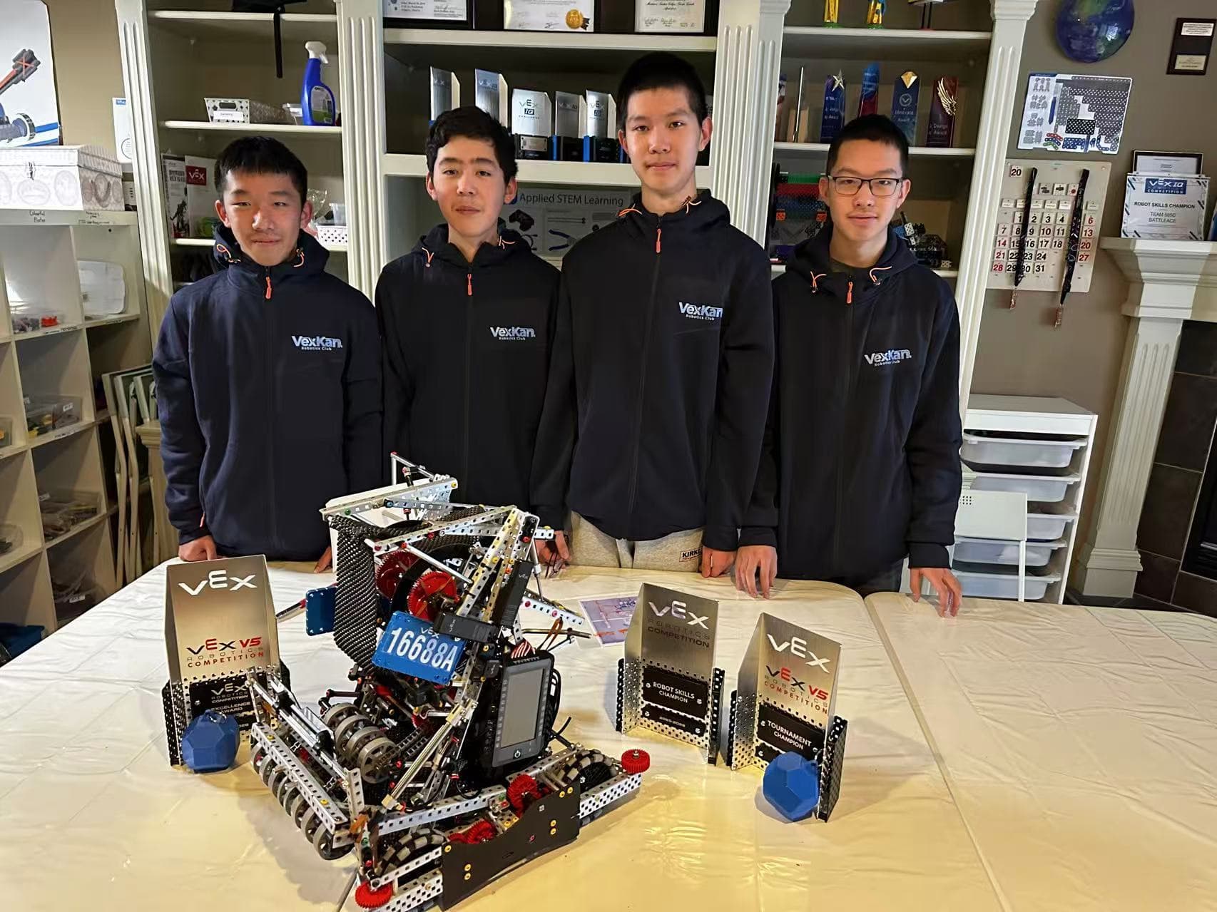 The four members of 16688A standing behind their V5 robot and its awards, the team number on the robot's plate.