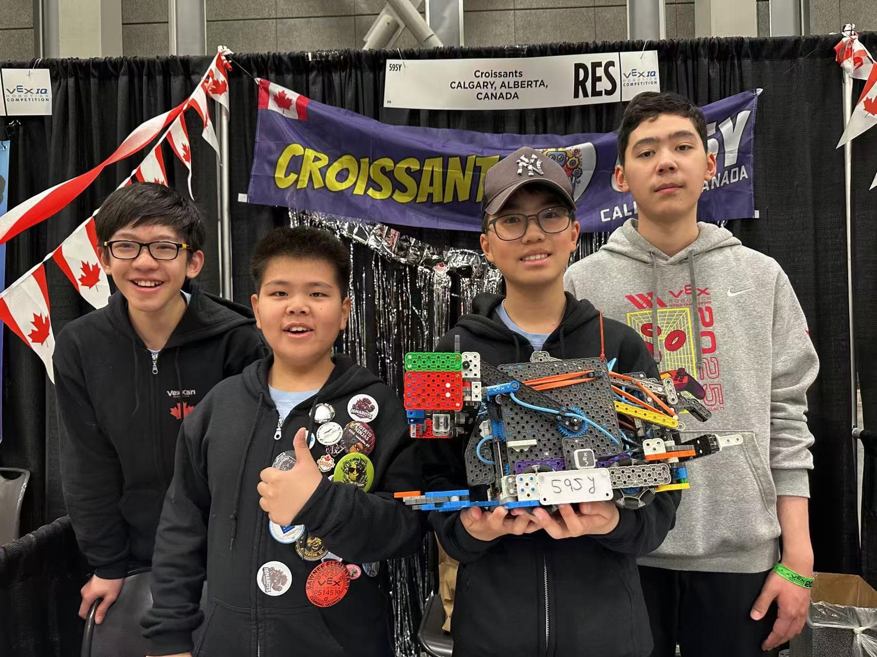 Four clubbers at their pit at a championship, holding up their VEX IQ robot in front of the team's banner.