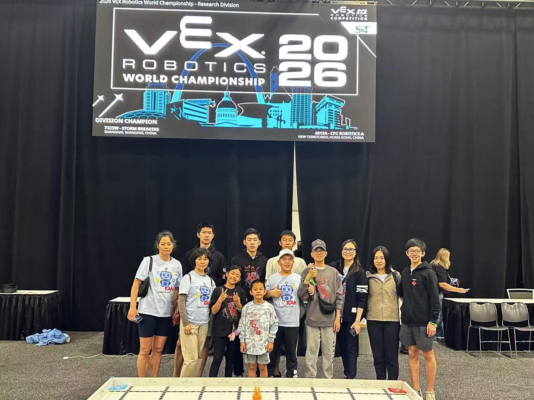 Clubbers and families standing together in front of the World Championship screen at the end of the event.