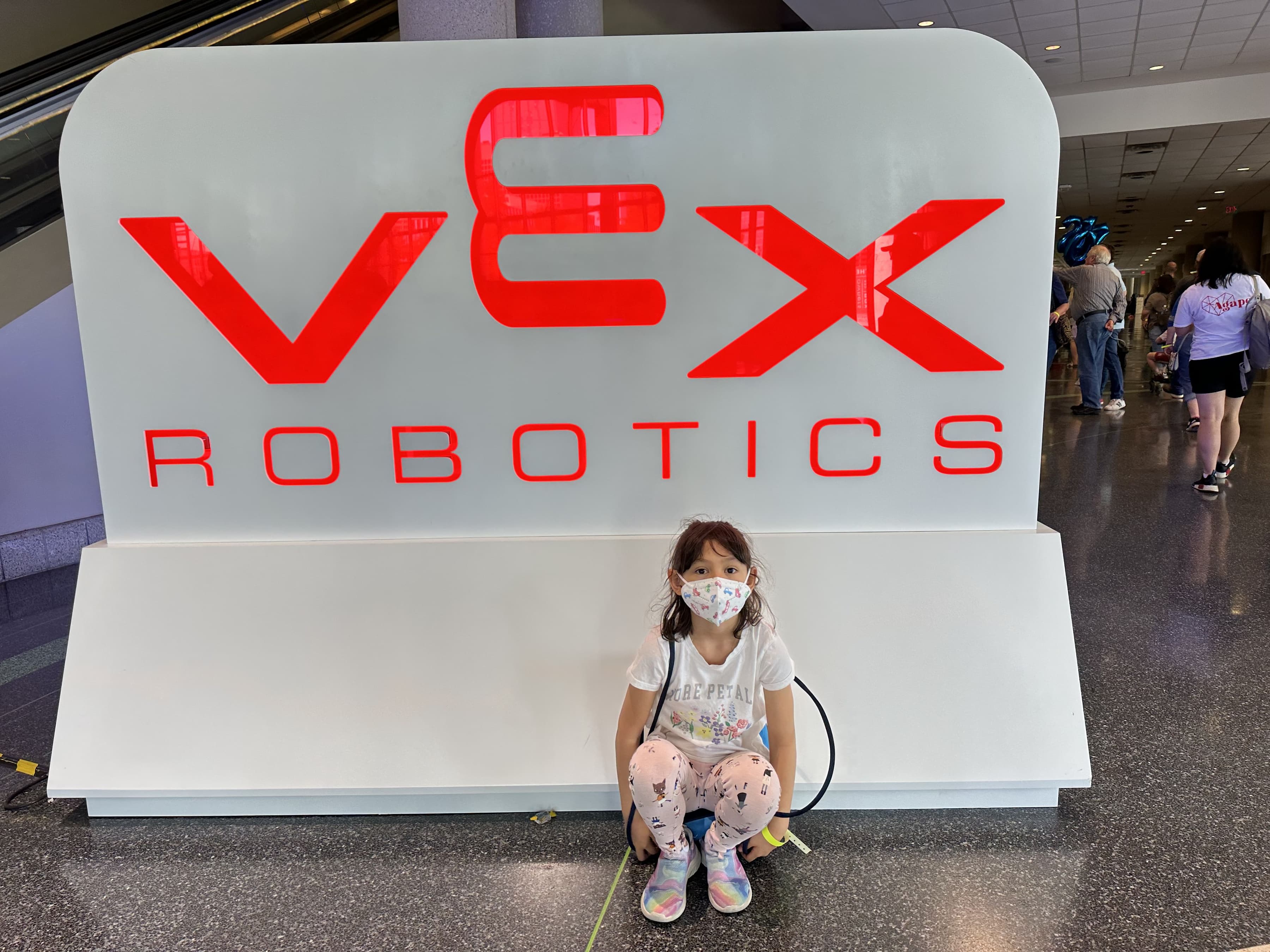 A young clubber crouched in front of a large VEX Robotics sign in the concourse at the World Championship.
