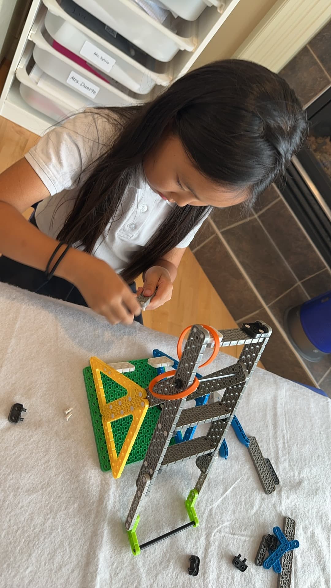 A young girl fitting a beam onto a VEX IQ frame at a table spread with parts.