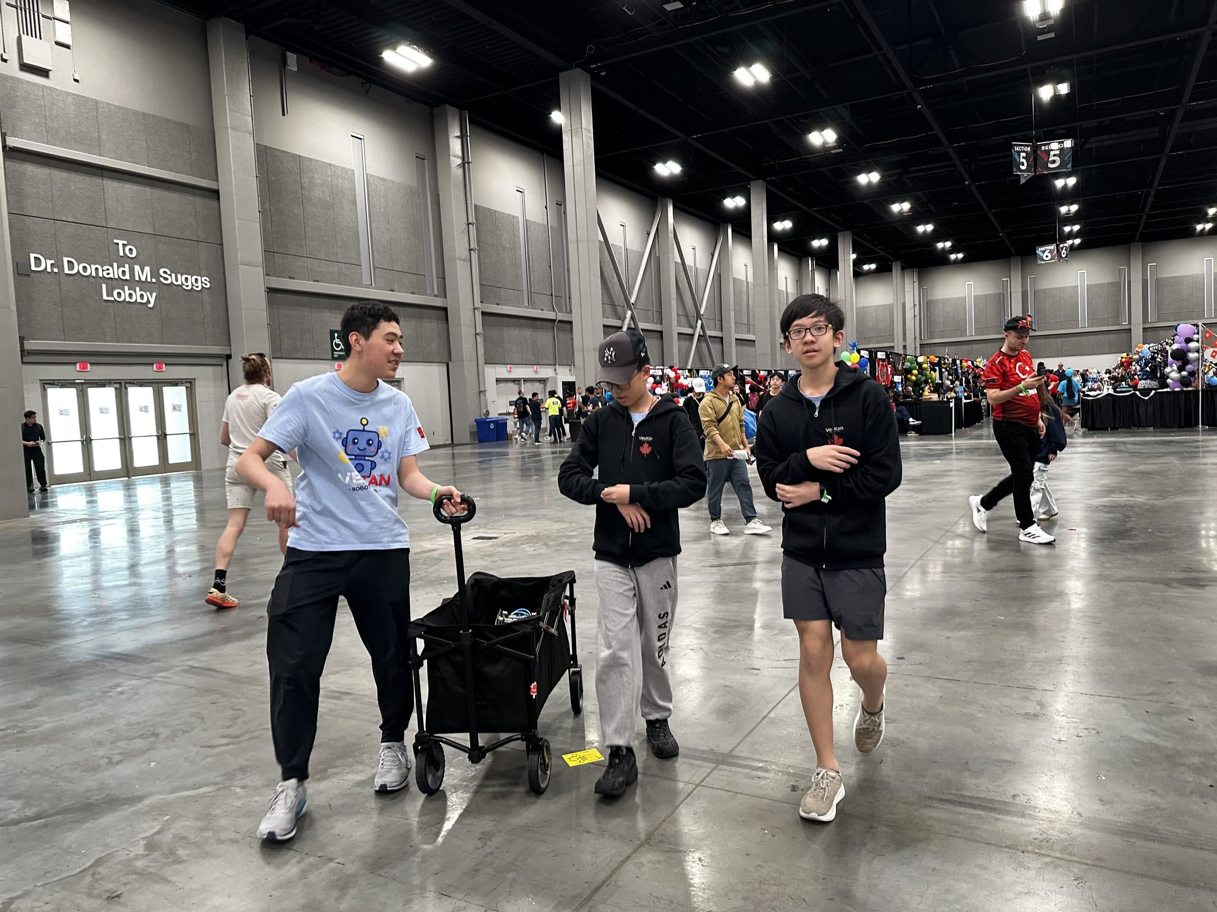 Three clubbers crossing the empty concourse of the convention centre, pulling the wagon that carries the robot and the toolkit between halls.