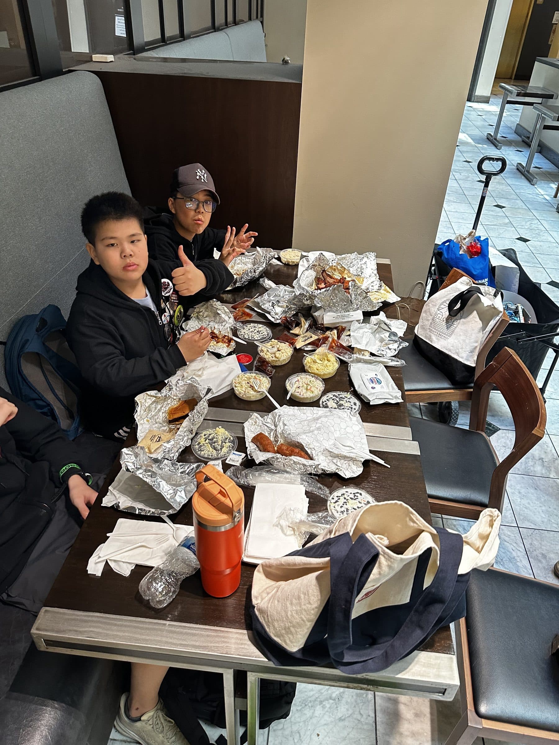 Two clubbers at a table covered in foil takeaway containers, one giving a thumbs up mid-meal.