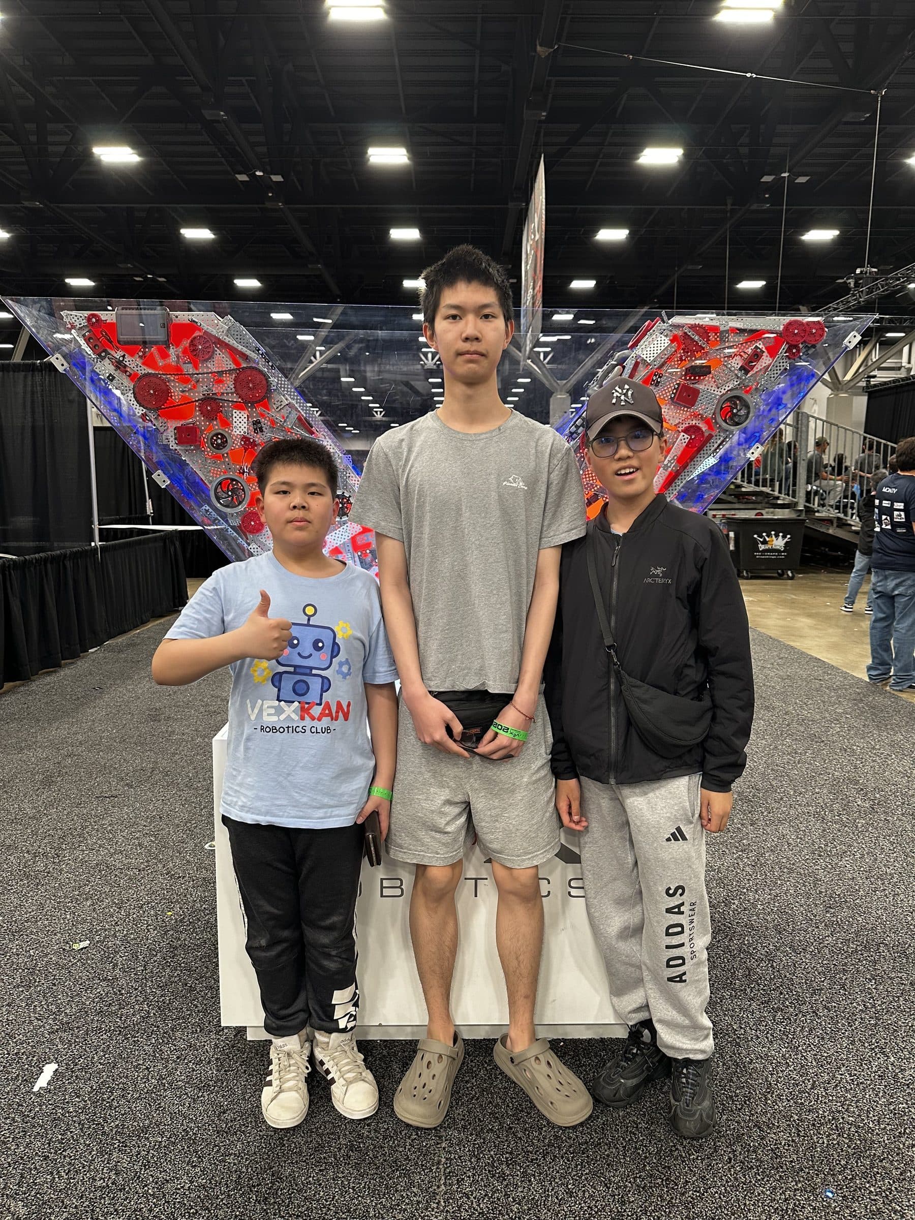 Three clubbers standing together in front of the large lit VEX Robotics sculpture on the competition floor.